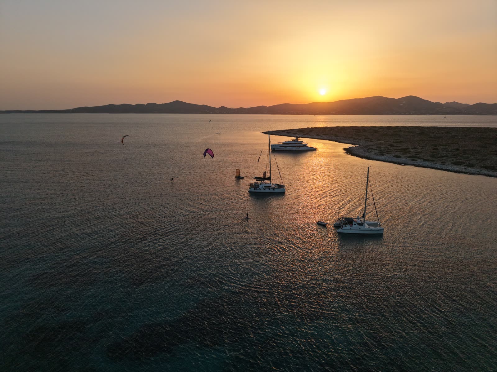 Sailboats at anchor beneath an orange sunset